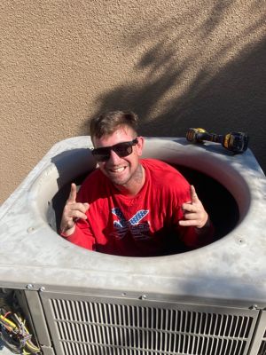 A NexGen Tech sitting inside an AC condensor unit smiling