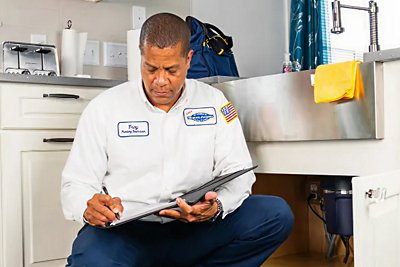 Plumber in kitchen writing in notebook