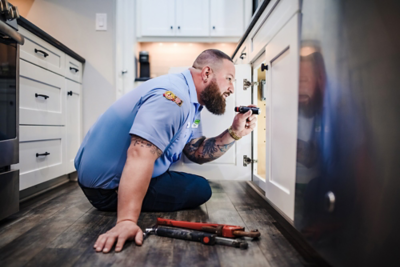 Drain cleaning expert from Plumbing Today using a flashlight to inspect under a sink