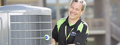 Technician smiling behind an air conditioner - Williams Comfort Air Heating, Cooling, Plumbing & More