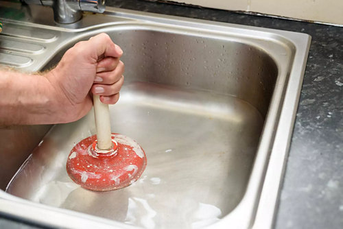 Technician using plunger to clear a clogged sink