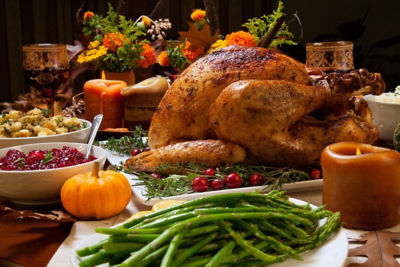 A Thanksgiving dinner spread that includes turkey, green beans, cranberries and stuffing on the table with candles.