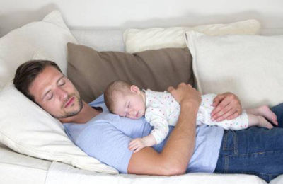 Man sleeping on sofa with baby on chest
