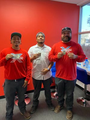 Three techs holding cash in front of a red wall