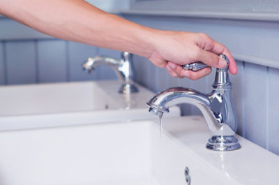 hand man opening silver faucet or water tap with white washing sink in public toilet.