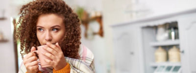 Young woman wrapped in blanket drinking hot tea