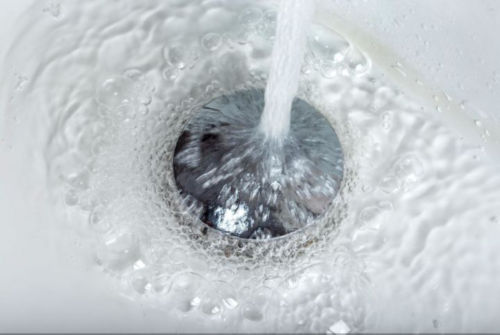 Close up overhead view of a wet metal drain in a white sink.