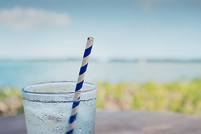 A glass of water with a blue striped straw, on a table with the Florida bay in the background