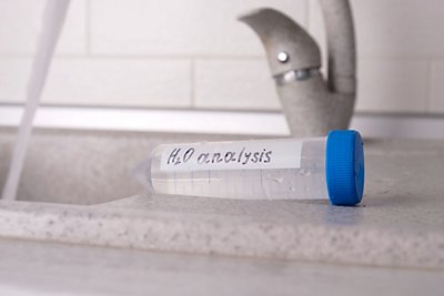 Analysis of tap water in the house, a test tube with a sample for a laboratory test close-up against the background of a faucet in the kitchen