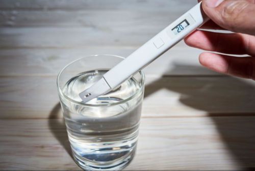 Hand holding a white thermometer in a small glass of water