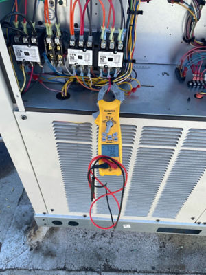 An opened AC unit with a Fieldpiece tool hooked up to wires.