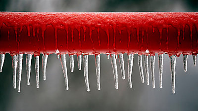 Frozen red pipe with icecycles on bottom