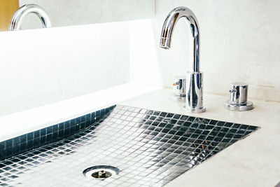 A modern bathroom sink with a mosaic tile basin, chrome faucet, and drain that could become clogged without proper Dallas plumber maintenance.