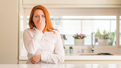 Red-headed woman wondering why her kitchen drain smells so bad.