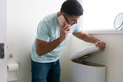 A side-view shot of a man standing in his bathroom looking at his toilet, there is a problem, he is on the phone trying to call a plumber.