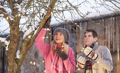 Woman and man bundled up and hanging lights on tree in yard