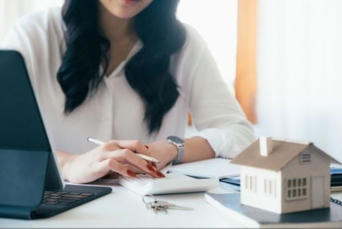 Dark-haired woman wearing white shirt calculating expenses.