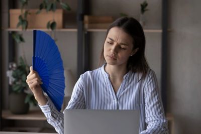 A woman fanning herself in front of her laptop.