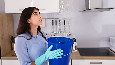 Woman in kitchen holding bucket catching water from leak