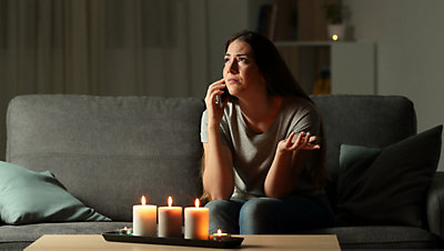 Distressed woman sitting on couch in dark with candles
