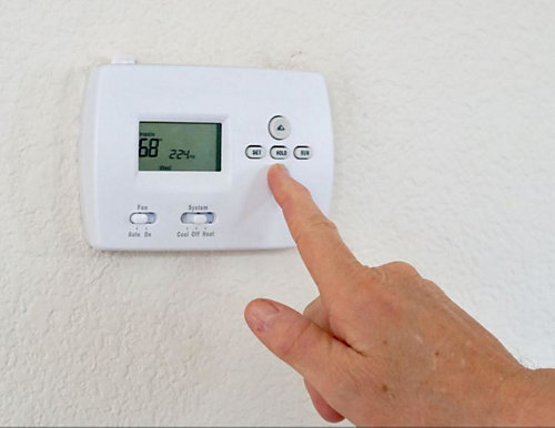 A person pressing a button on a thermostat
