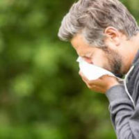 Man outside sneezing into tissue