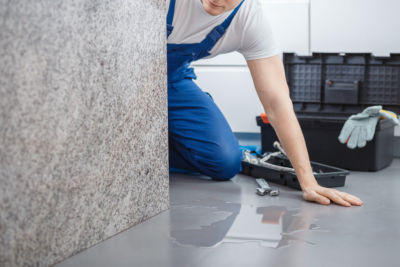 Plumber with toolbox looking at water on the floor from broken dishwasher