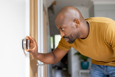 African American man adjusting the temperature on the thermostat of his house - home automation concepts