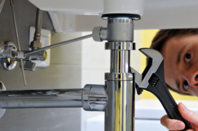 Man looking under sink at pipe with wrench in hand