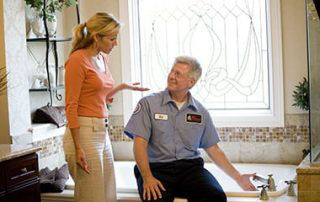 Plumber sitting down on tub talking to customer