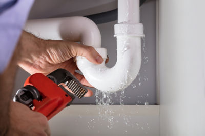 Plumber repairing leaking pipe beneath sink