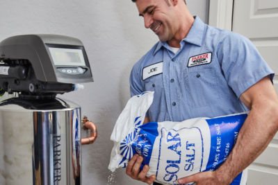 water technician adding salt into a water softerner system