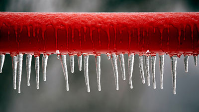 Frozen red pipe with icecycles on bottom