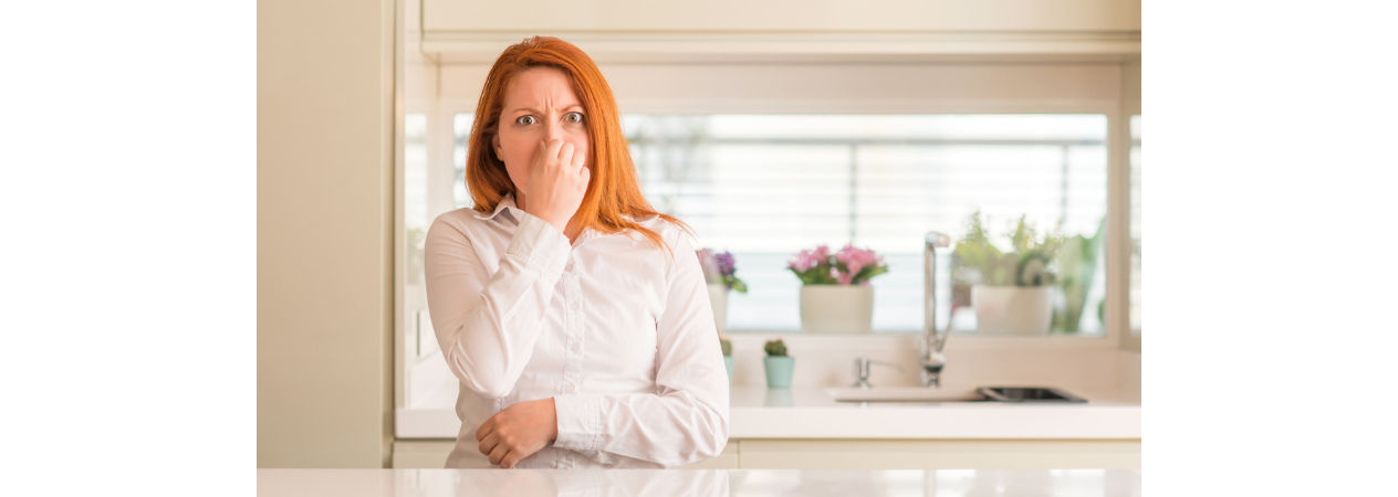 Woman with disgusted look holding her nose in front of kitchen sink